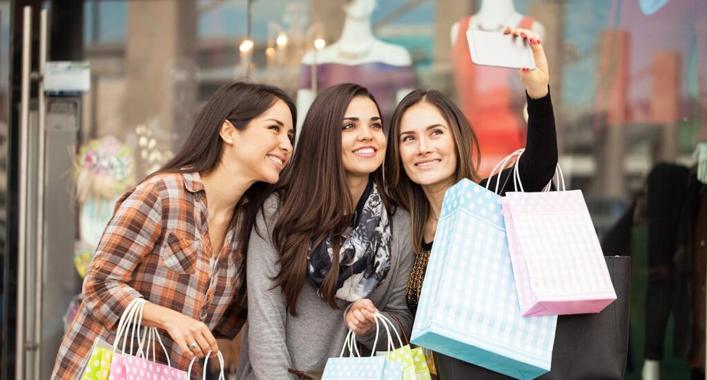 Three young woman carrying shopping bags taking a selfie