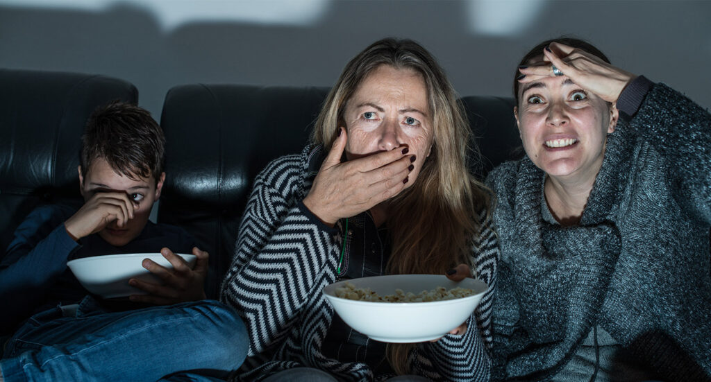 Two woman and a child with frightened expressions watching a movie with popcorn